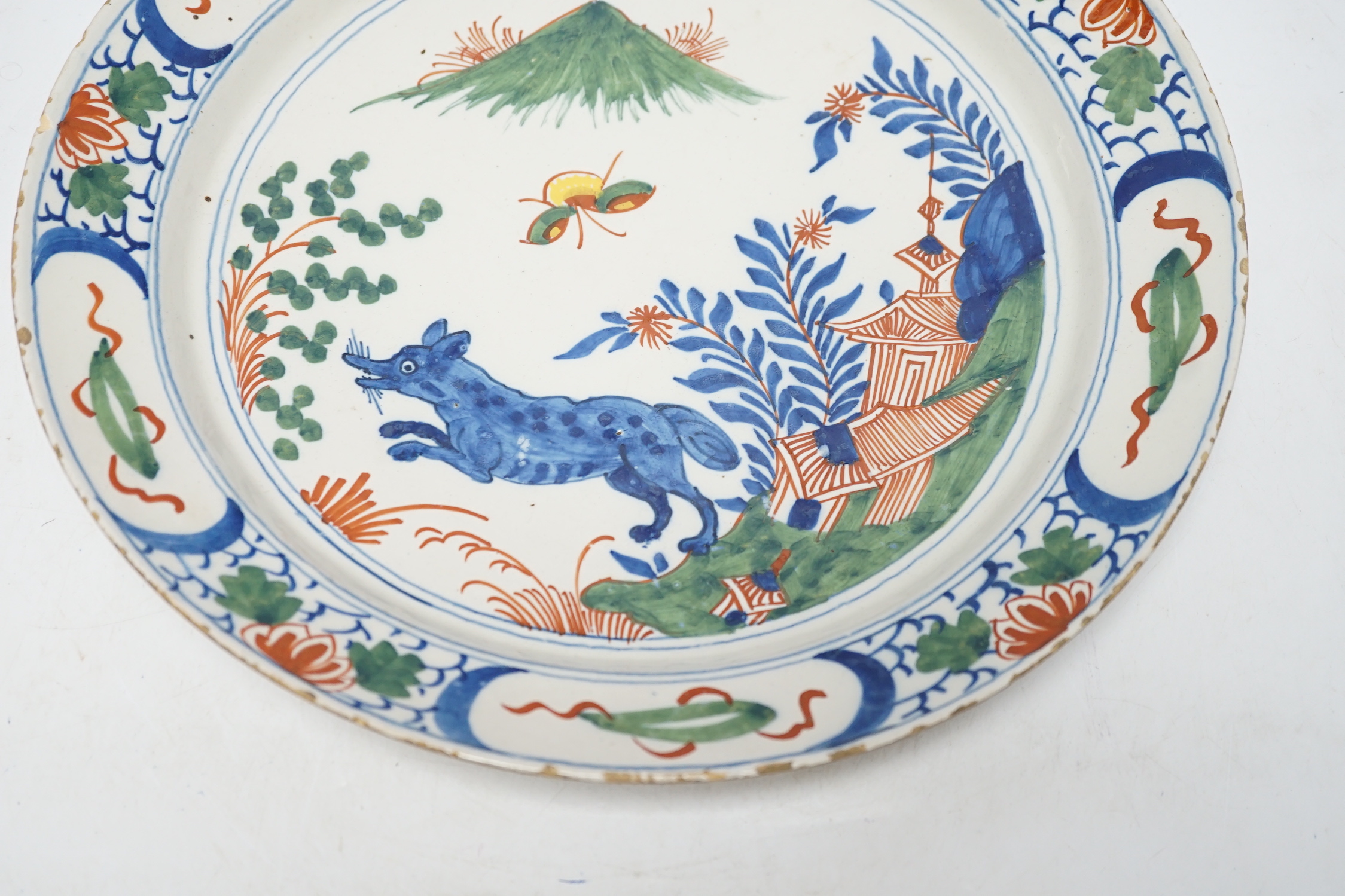 An 18th century Delft dish, the centre painted with a wolf, a bee and a pavilion, 35cm